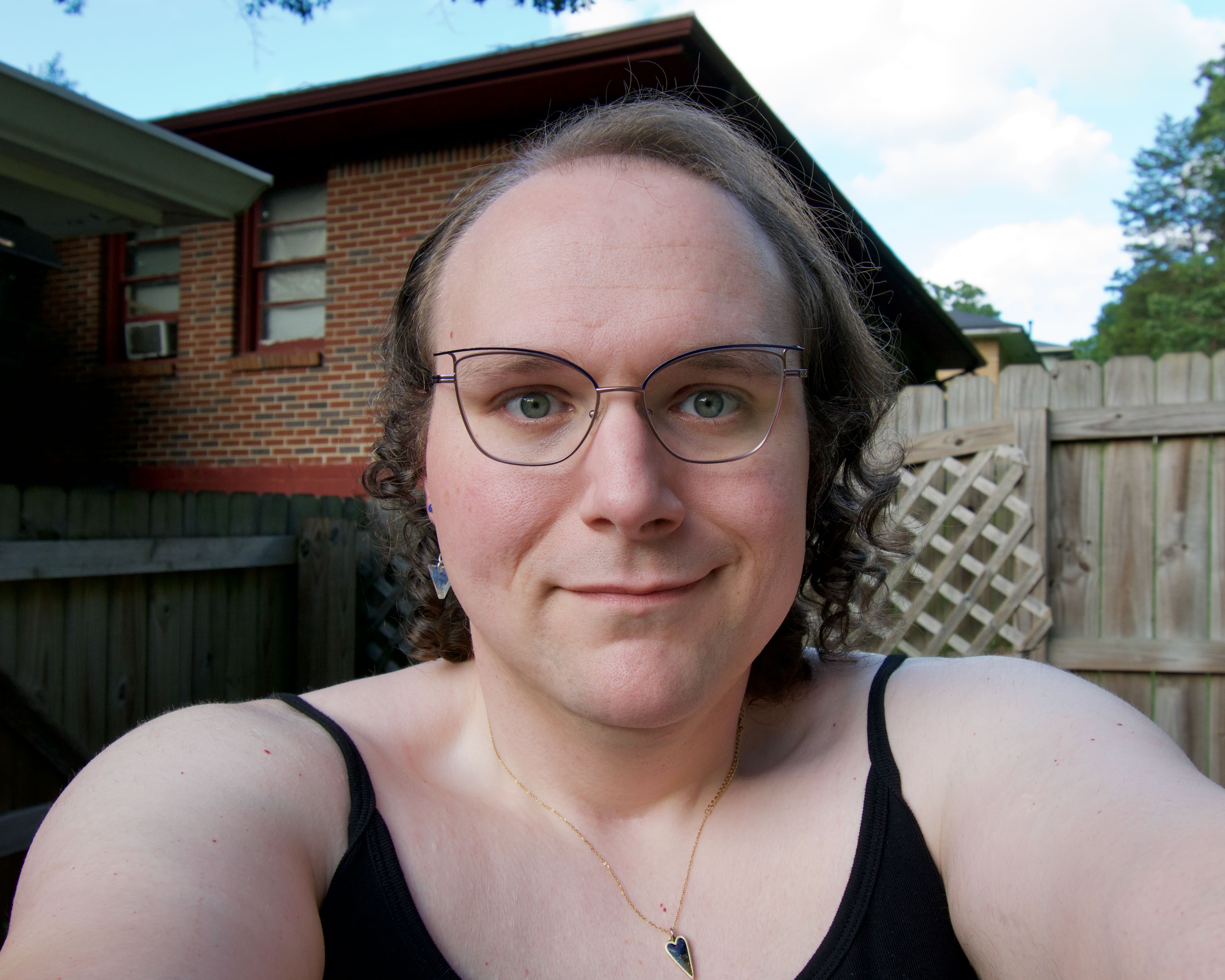 A wide-angle selfie of a woman, smiling at the camera. She is wearing glasses and some jewelry.