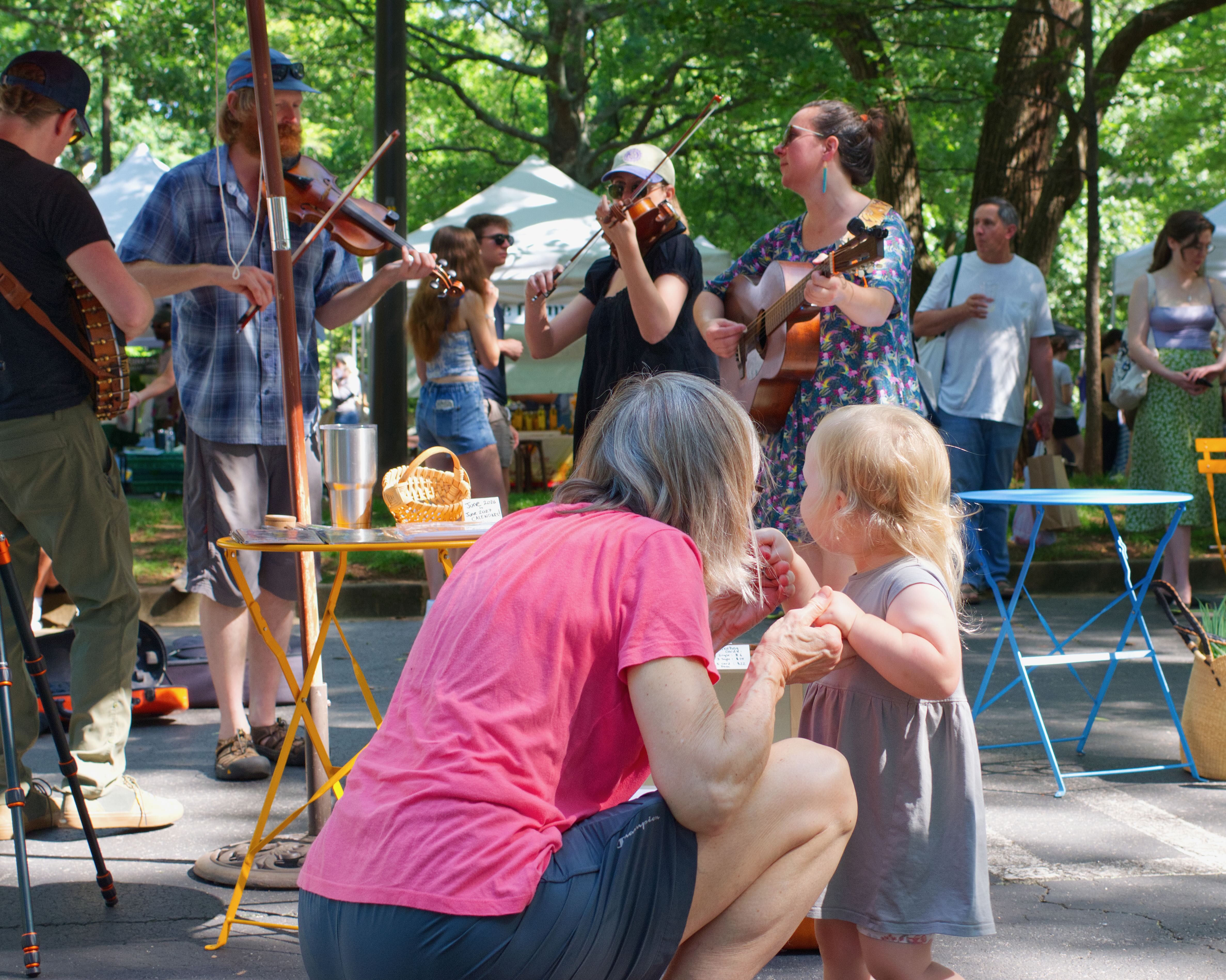 A little girl looks on with a loved one as old time musicians play at the farmers market.